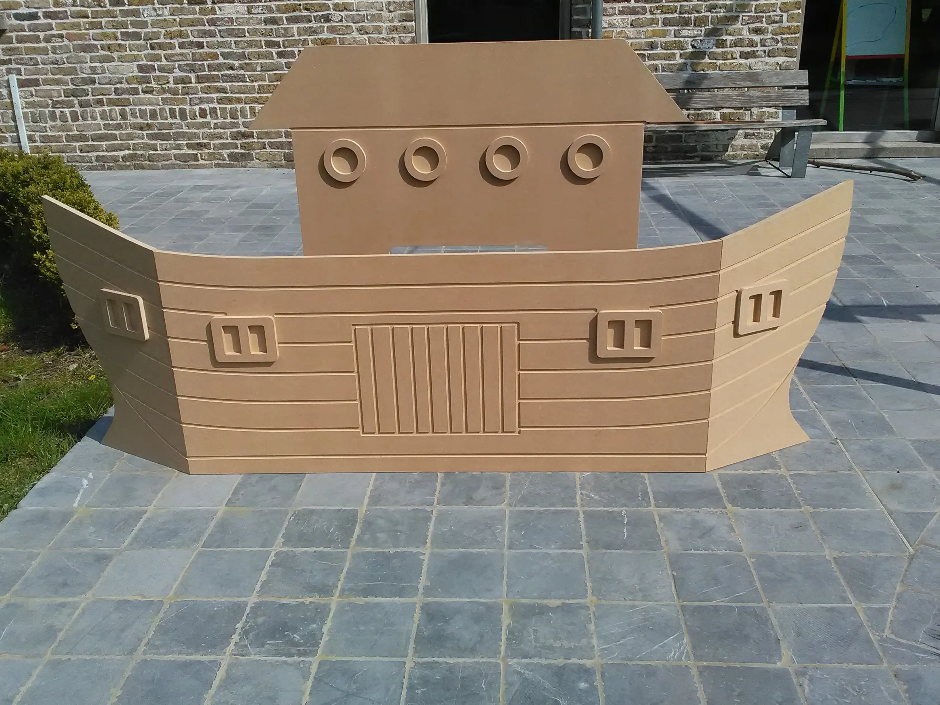 Verticale MDF-platen in de vorm van een schip. Het stelt de ark van Noah voor. Dit werd gebruikt voor de eerste communie in de kerk. Het bestaat uit twee delen: een schip vooraan met de kajuit erachter. Totaal 2.5m breed en 1.4m hoog. Inklapbaar zodat het in een auto past.